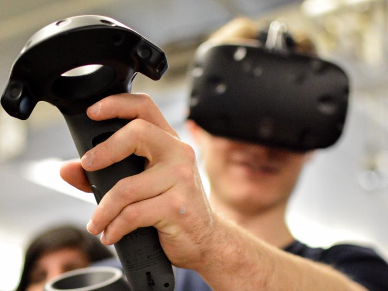 Student holding up virtual reality joystick and testing virtual reality environment.