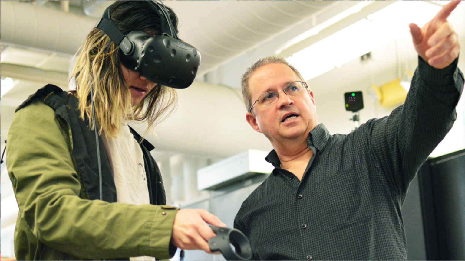 A professor points as a student wears a virtual reality headset.