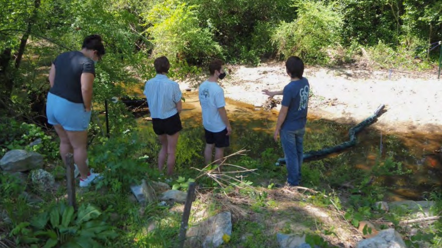 Students standing by their Happy Crawfish invention by a creek.