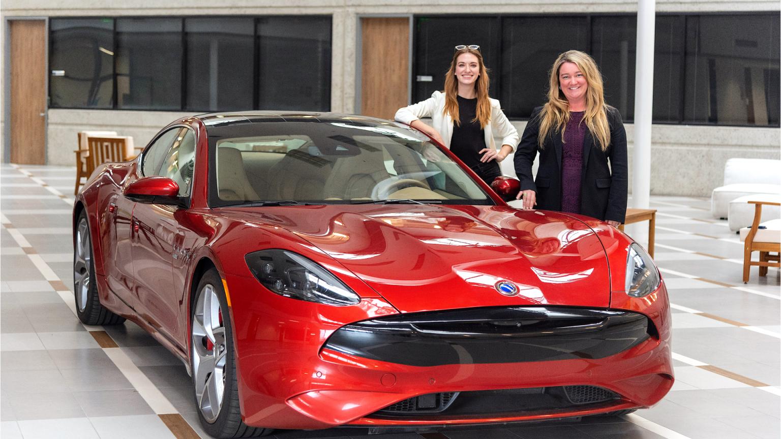 Jenn Voelker and Julia Vorpahl are standing next to a red car designed by Karma Automotive.