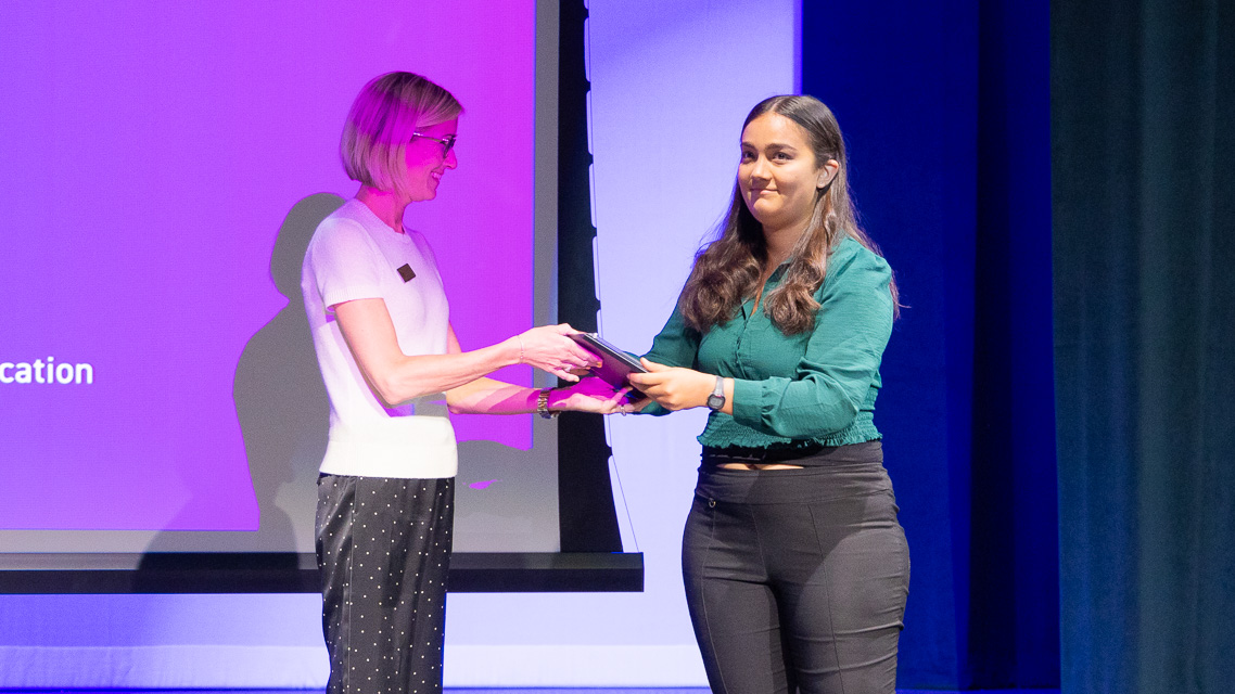 Karina Bhattacharya receiving a plaque on-stage at the Three-Minute Thesis competition.