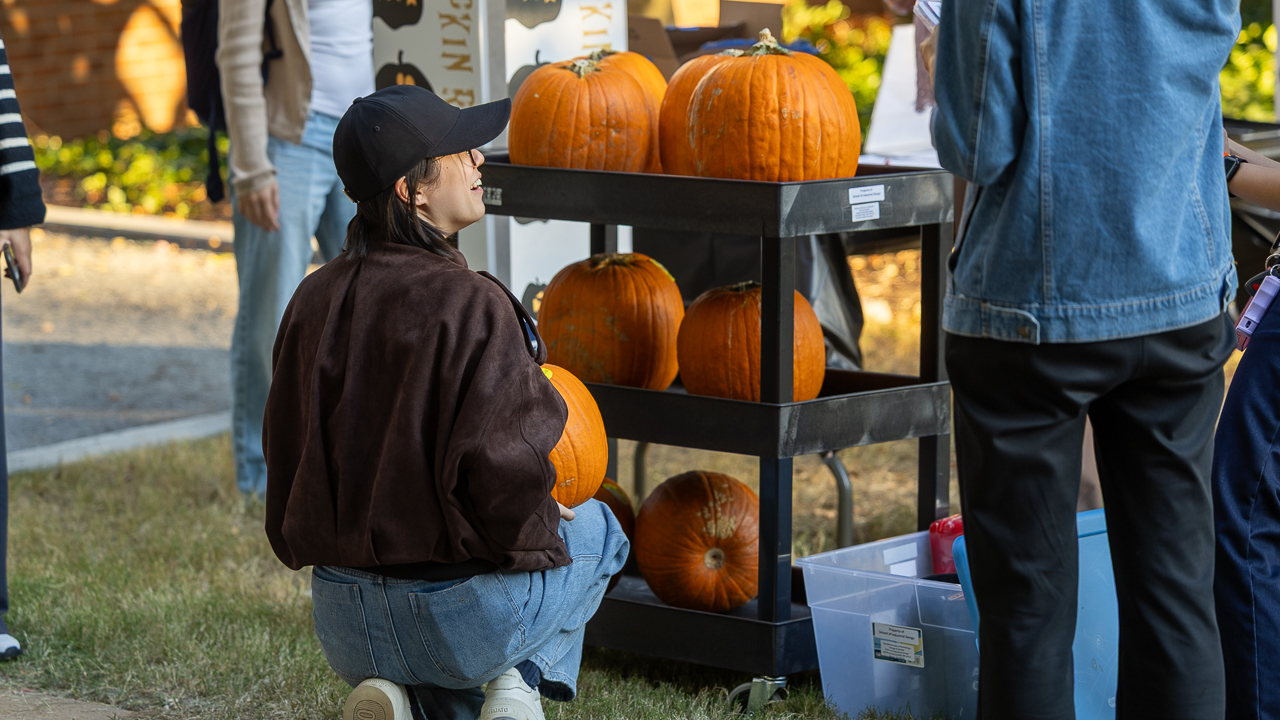 Student holds pumpkin next to cart stacked with pumpkins at the event start