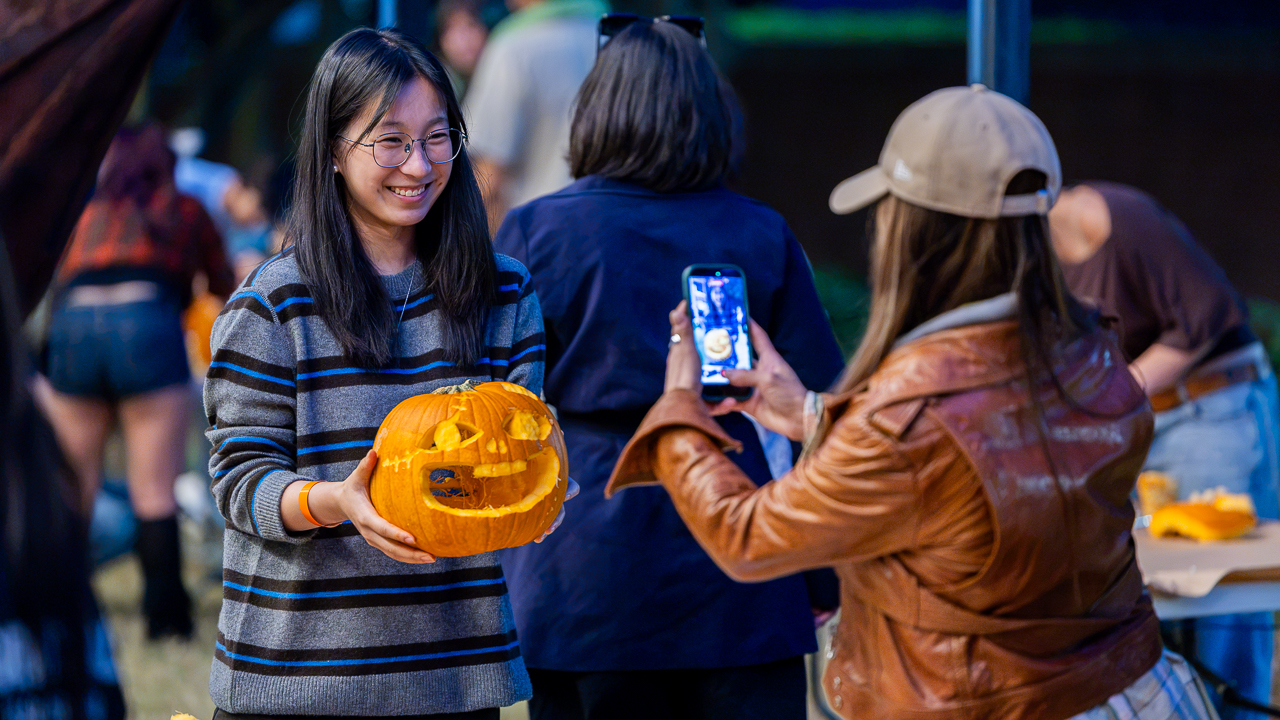 Student poses with her finished pumpkin as another takes a photo